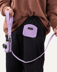 Person holding a purple leash with a matching pouch, wearing a brown sweatshirt and black pants.