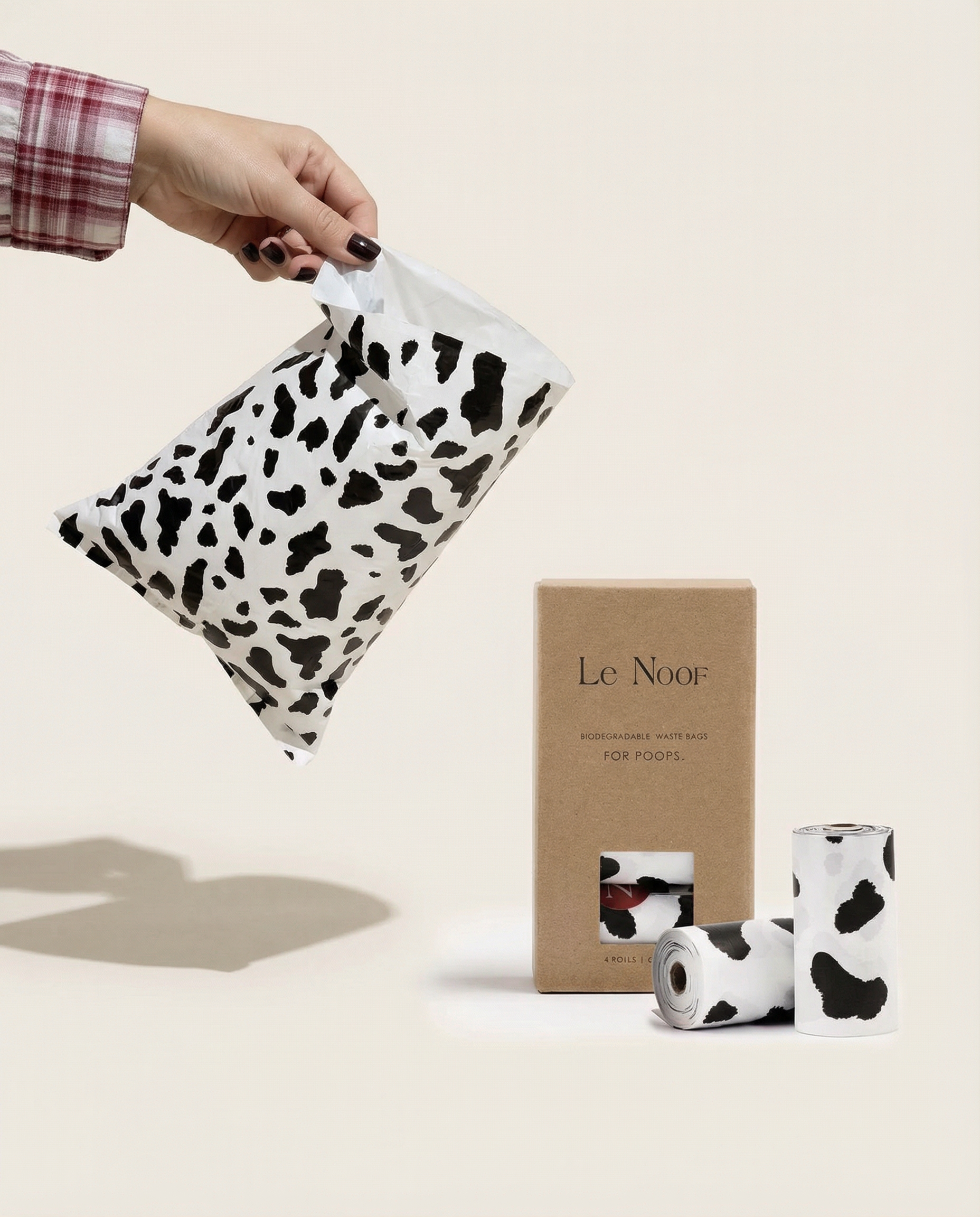 Cow print biodegradable dog poop bags held in hand, Le Noof