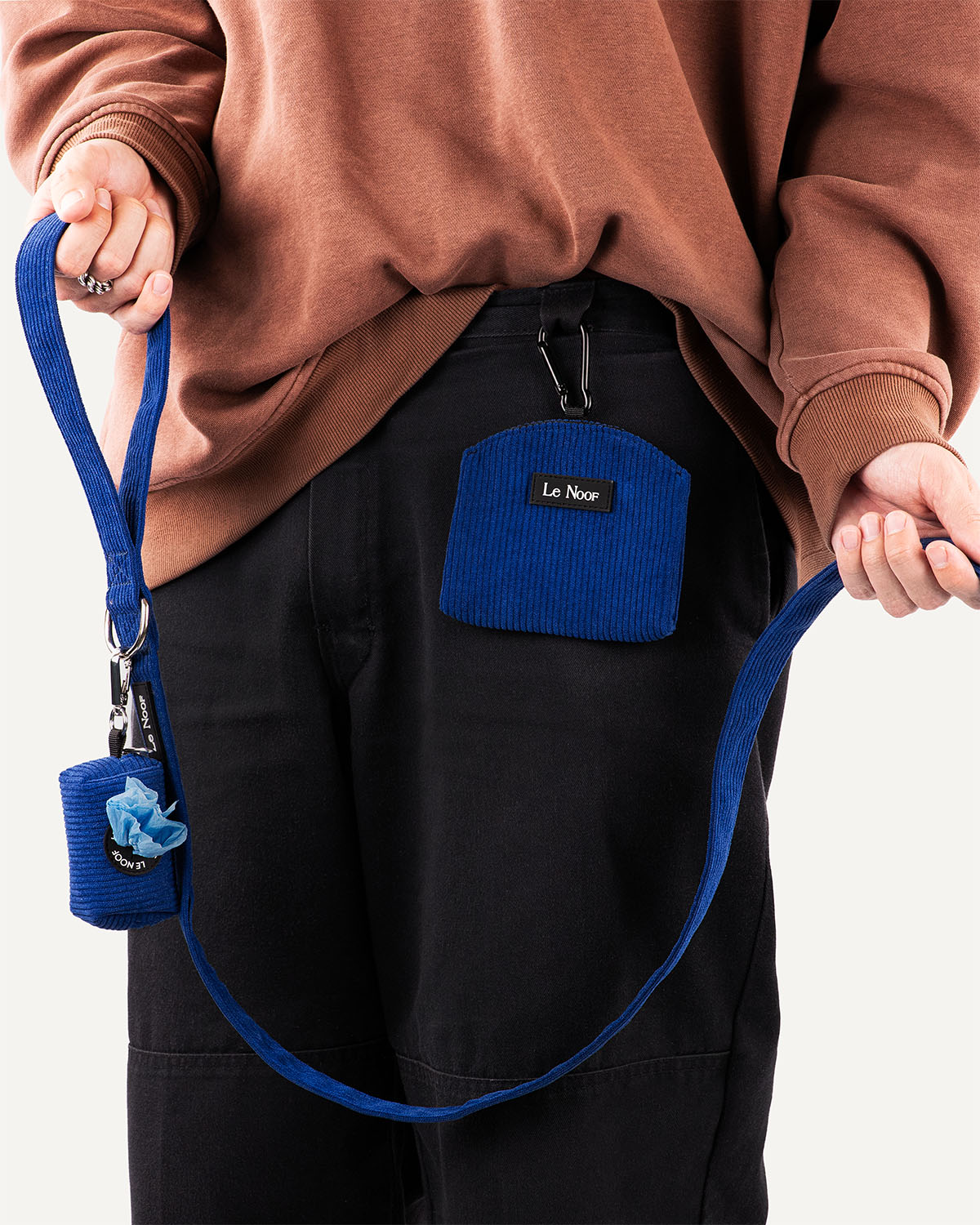 person holding blue corduroy dog leash with poop bag holder attached and treat pouch clipped to pants