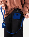 person holding blue corduroy dog leash with poop bag holder attached and treat pouch clipped to pants