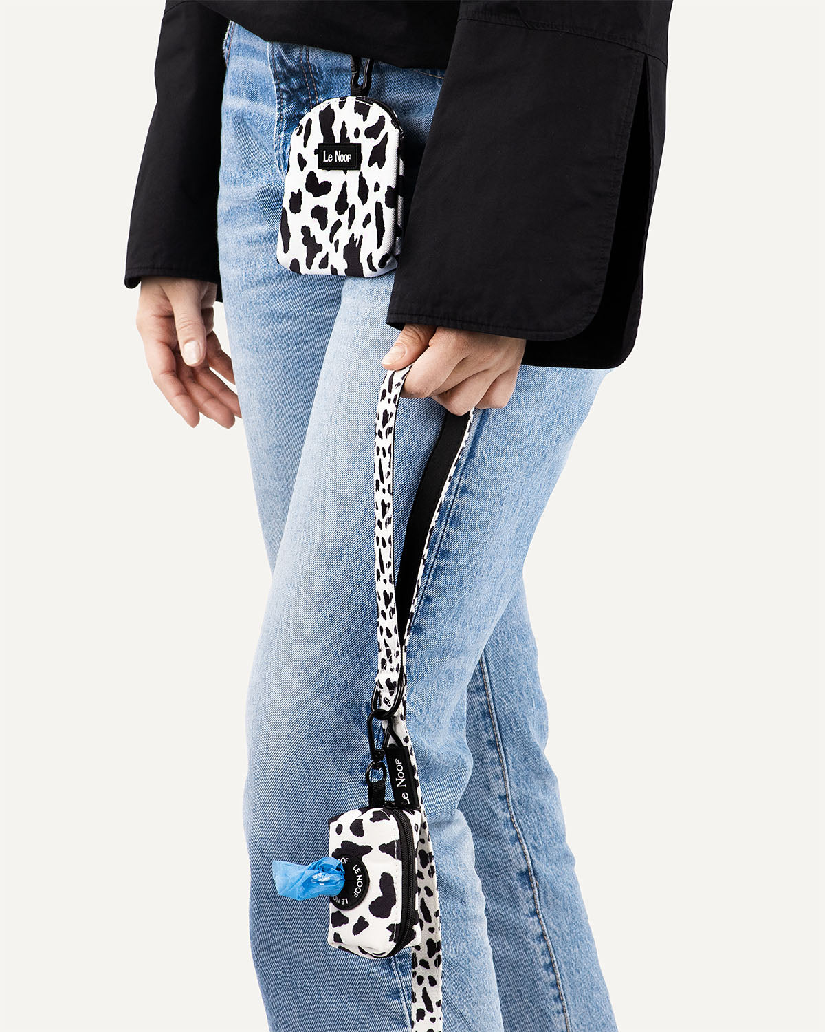 woman holding cow print dog leash with matching poop bag holder clipped to it and woman wearing matching dog treat pouch