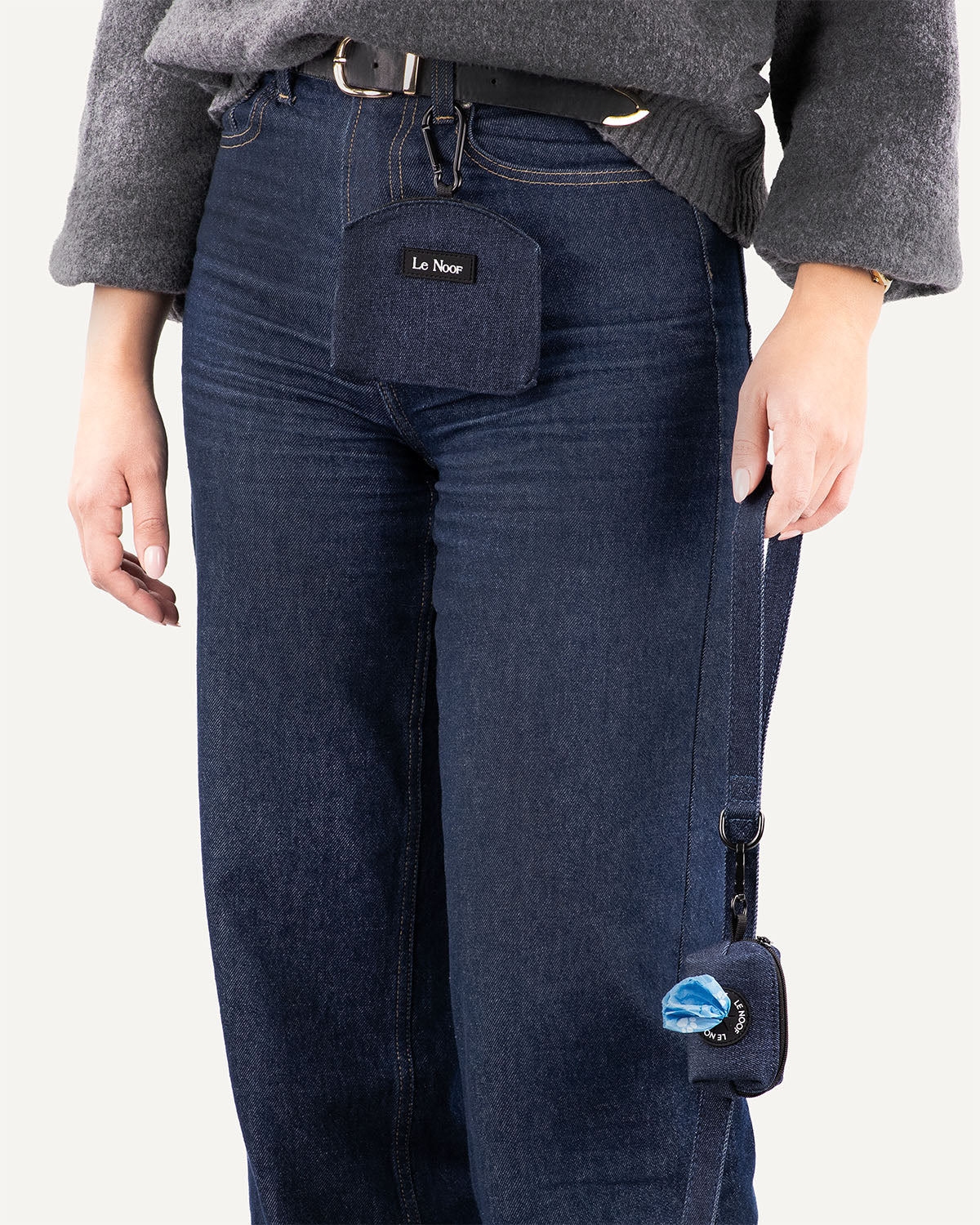woman holding dark blue denim dog leash with poop bag holder clipped to the leash and woman wearing matching dog treat pouch