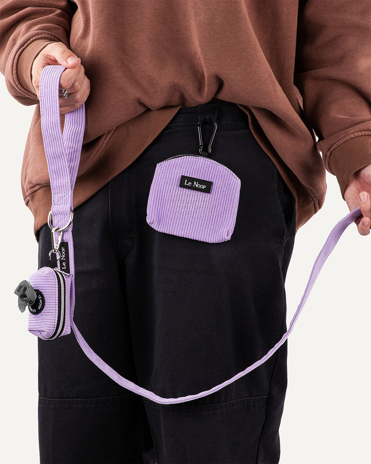 Person holding a purple leash with a matching pouch, wearing a brown sweatshirt and black pants.