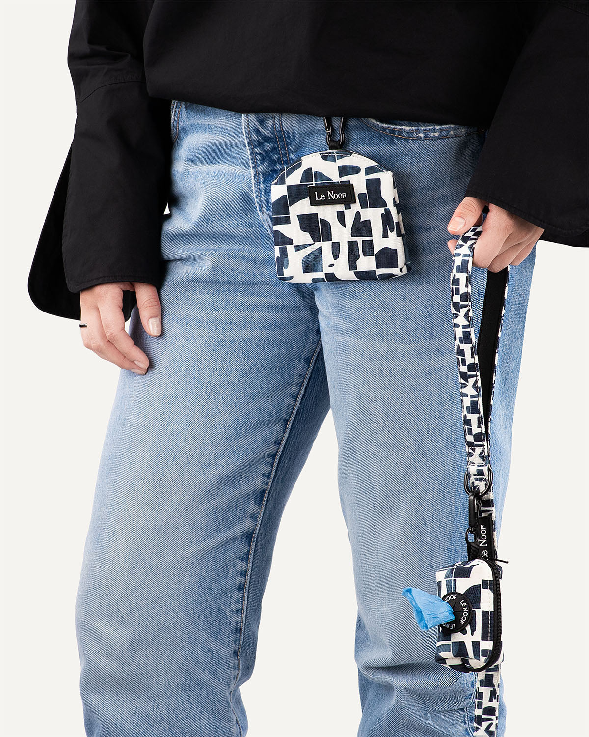 Person holding modern geometric print dog leash with matching poop bag holder attached to it and dog treat pouch clipped to jeans
